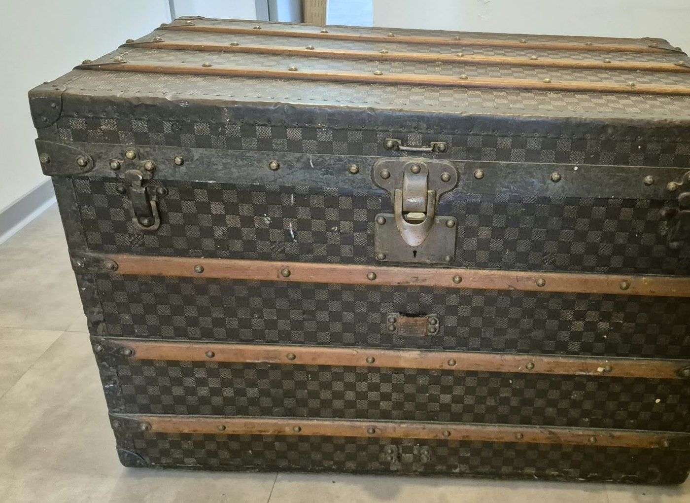 Malle de voyage à toile damier, cerclée de lattes de bois et cloutée