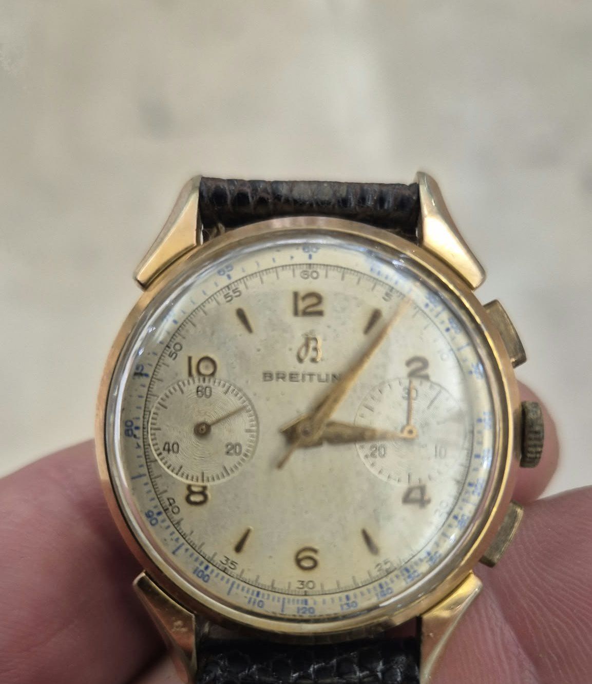 Chronographe Breitling à cadran crème et bracelet de cuir noir, tenu dans la main