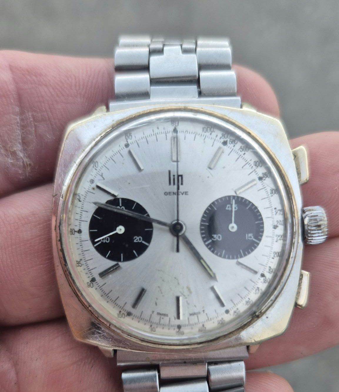 Chronographe Lip à cadran argenté et compteurs noir et gris, bracelet acier, tenu dans la main