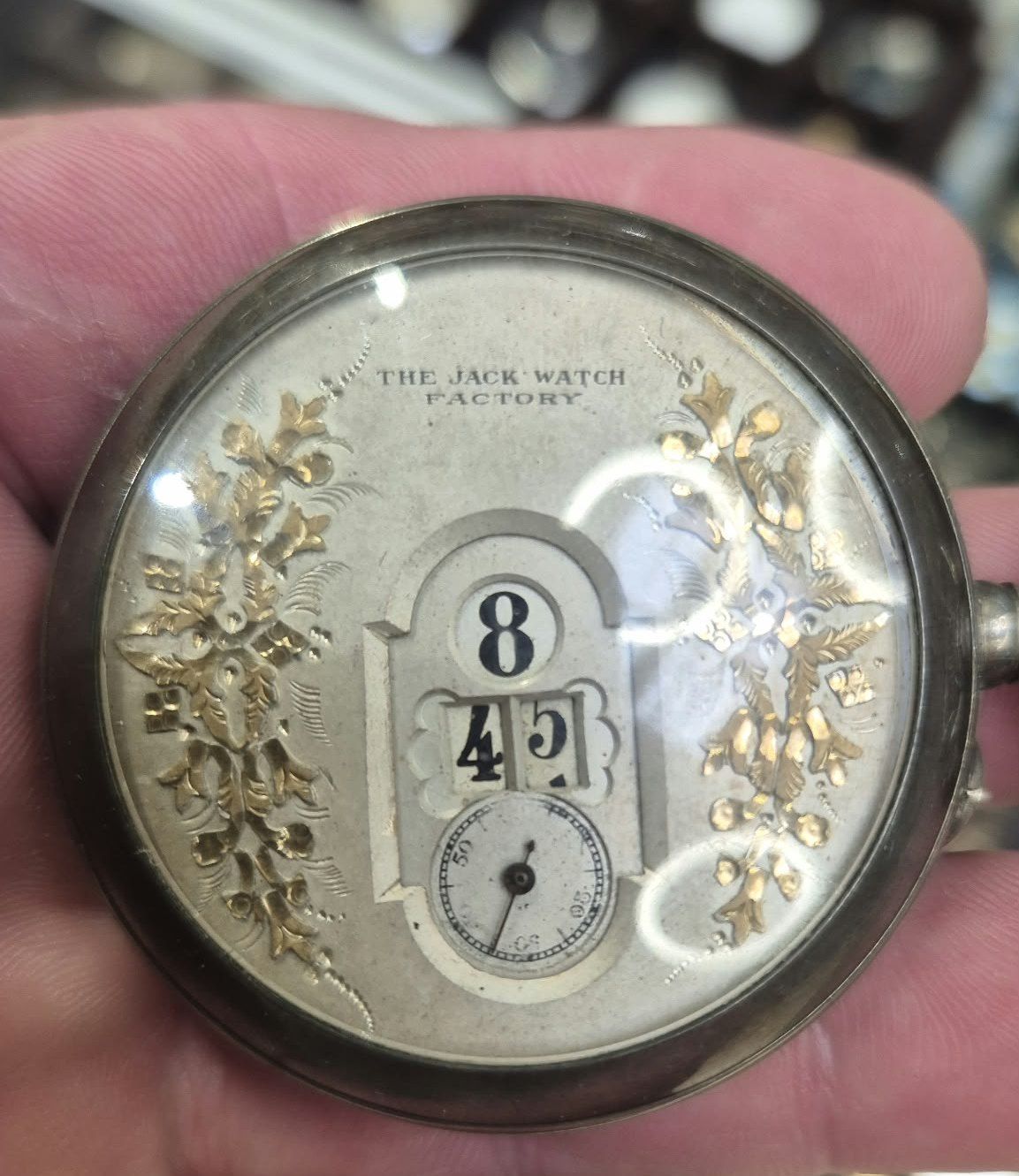 Montre de poche à heures sautantes, cadran argenté orné de feuillages dorés, tenue dans la main